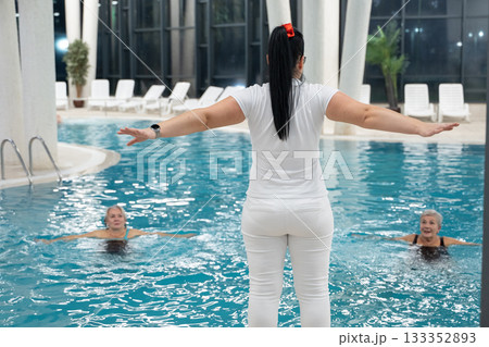Instructor leading aquatic fitness training for group senior women in a swimming pool. Concept of health, exercise, wellness, water therapy, and active aging lifestyle 133352893
