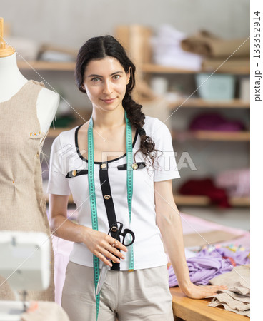 Female tailor with scissors standing next to mannequin in sewing studio 133352914