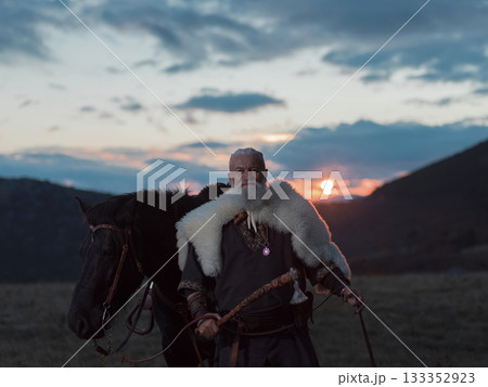 A Viking warrior on a large black horse surveys a dramatic landscape during sunset, wearing a fur cloak. The scene evokes ancient exploration, adventure, and the spirit of the wild. A Viking warrior on a large black horse surveys a dramatic landscape during sunset, wearing a fur cloak. The scene evokes ancient exploration, adventure, and the spirit of the wild. 133352923