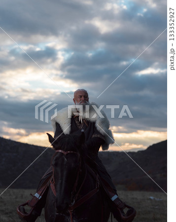 A Viking warrior on a large black horse surveys a dramatic landscape during sunset, wearing a fur cloak. The scene evokes ancient exploration, adventure, and the spirit of the wild. A Viking warrior on a large black horse surveys a dramatic landscape during sunset, wearing a fur cloak. The scene evokes ancient exploration, adventure, and the spirit of the wild. 133352927