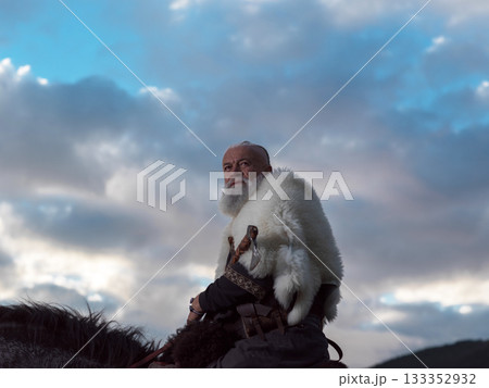 A Viking warrior on a large black horse surveys a dramatic landscape during sunset, wearing a fur cloak. The scene evokes ancient exploration, adventure, and the spirit of the wild. A Viking warrior on a large black horse surveys a dramatic landscape during sunset, wearing a fur cloak. The scene evokes ancient exploration, adventure, and the spirit of the wild. 133352932