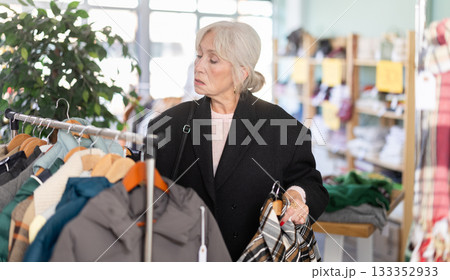Mature woman chooses fashionable coat or jacket in clothing store Mature woman chooses fashionable coat or jacket in clothing store 133352933