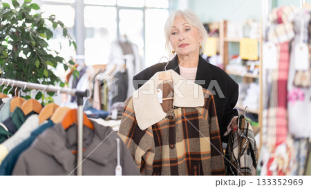 Mature woman chooses fashionable coat or jacket in clothing store Mature woman chooses fashionable coat or jacket in clothing store 133352969