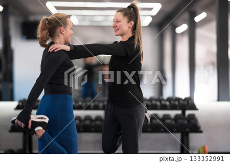 Two women engage in a friendly stretching exercise at a gym during a workout session in the morning Two women engage in a friendly stretching exercise at a gym during a workout session in the morning 133352991