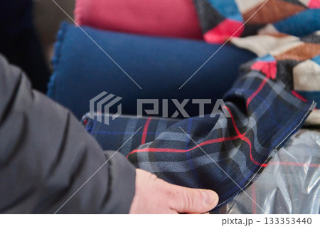 Close up of a plaid scarf with a hand, studio shot of a soft textile, colorful cushions in the background, product photo, fashion accessory Close up of a plaid scarf with a hand, studio shot of a soft textile, colorful cushions in the background, product photo, fashion accessory 133353440