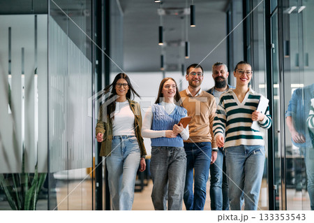 Group of young business team walking together through a modern office hallway, smiling and discussing work. Concept of confidence, teamwork, leadership, and positive workplace culture. Group of young business team walking together through a modern office hallway, smiling and discussing work. Concept of confidence, teamwork, leadership, and positive workplace culture. 133353543