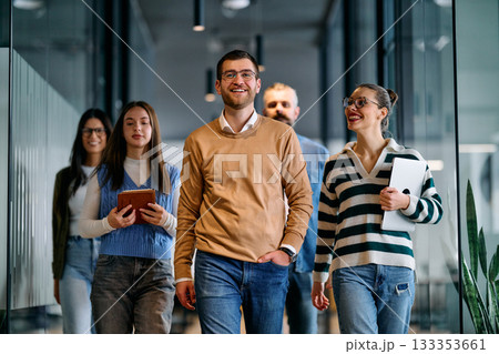 Group of young business team walking together through a modern office hallway, smiling and discussing work. Concept of confidence, teamwork, leadership, and positive workplace culture. 133353661