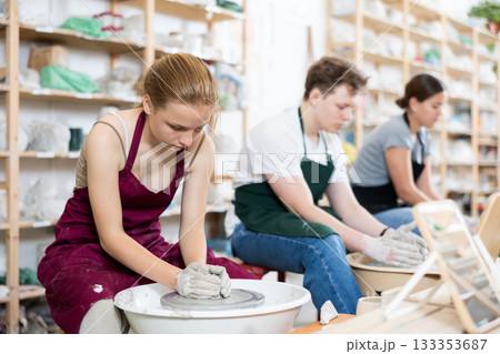 Young woman teacher and two teenagers make products on potter's wheel 133353687