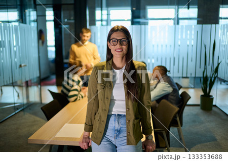 Confident business woman smiling while using smartphone during a team meeting in a modern office environment. Concept of communication, leadership, and professional confidence. 133353688