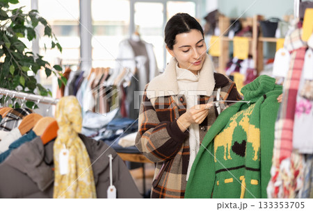 Girl chooses fashionable sweater in clothing store 133353705