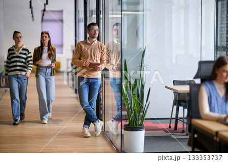 Businessman standing by glass wall in a modern office corridor, holding a digital tablet and smiling with reflection visible on the glass, symbolizing success, optimism, and modern business lifestyle. 133353737
