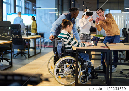 Diverse business team collaborating in a modern office environment. A woman in a wheelchair works on a laptop while colleagues explore virtual reality and digital tools, promoting innovation Diverse business team collaborating in a modern office environment. A woman in a wheelchair works on a laptop while colleagues explore virtual reality and digital tools, promoting innovation 133353750
