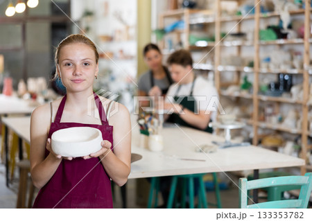 Teenage girl posing with ceramic bowl in ceramic workshop 133353782