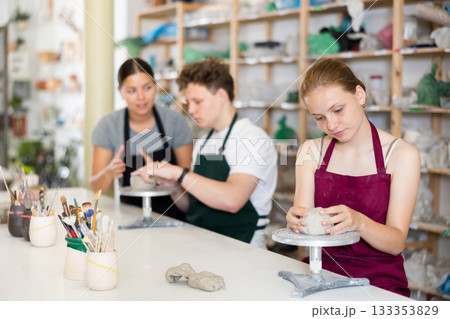 Young woman teacher helps teenagers boy and girl to sculpt ceramic product 133353829