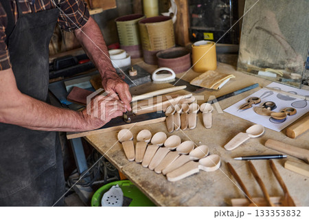 Craftsman carving wooden spoons in workshop, artisan shaping wood with hand tools, handmade crafts, traditional woodworking, small business, hobby project, craftsperson at work 133353832