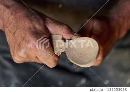 Close-up of hands carving a wooden spoon, woodworking craft, artisan creating handmade utensil, traditional carving process, hobby and craftsmanship, creating unique kitchenware. 133353928