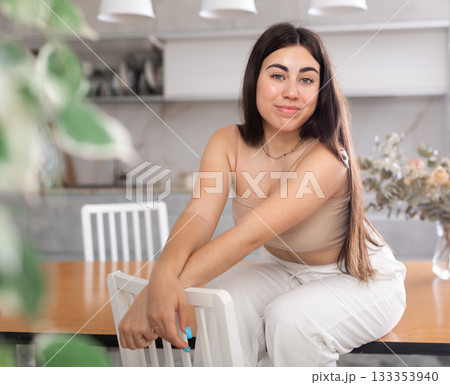 Smiling young woman posing sitting on kitchen table Smiling young woman posing sitting on kitchen table 133353940