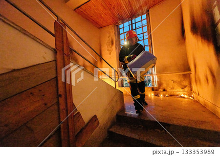 Brave firefighter carrying a rescued cat in a portable cage down smoky stairs during a building fire, symbolizing courage, compassion, and dedication to saving both human and animal lives in 133353989