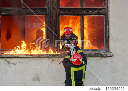 Brave firefighter rescuing a cat from a burning building, visible flames and smoke, dramatic scene, urban environment, emergency response, hero in action, saving lives 133354023