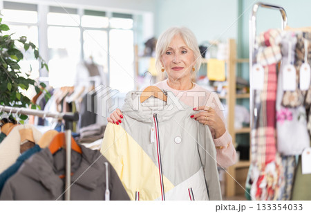 Mature woman chooses fashionable coat or jacket in clothing store Mature woman chooses fashionable coat or jacket in clothing store 133354033