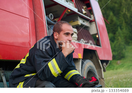 Thoughtful Firefighter in Uniform Sits on Firetruck, Contemplating Rescue Operations, Emergency Services, Fire Safety, Training, and Community Support, Surrounded by Nature 133354089
