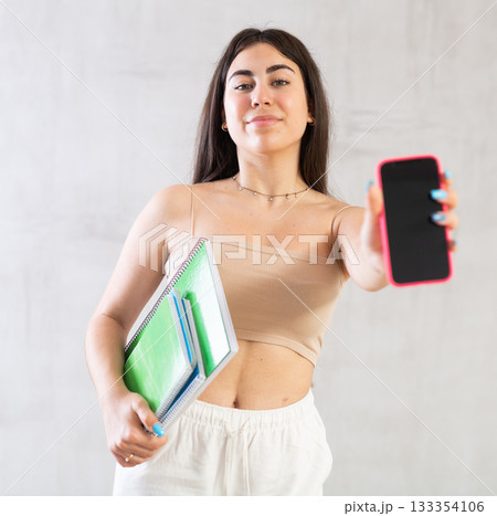 Young woman holding notebooks showing mobile phone Young woman holding notebooks showing mobile phone 133354106