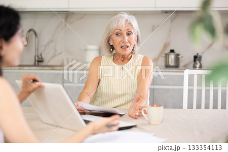 Elderly woman discussing deal with saleswoman in kitchen 133354113