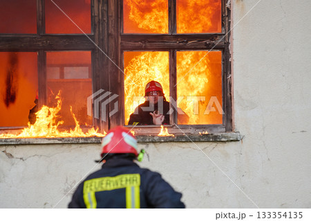 Brave firefighter rescuing a cat from a burning building, visible flames and smoke, dramatic scene, urban environment, emergency response, hero in action, saving lives 133354135