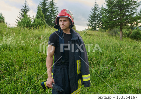 Portrait of a confident firefighter in helmet and uniform standing in a sunlit field, ready for action and emergency response, showcasing bravery and dedication. 133354167