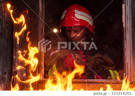 Firefighter rescuing a baby from burning building, fireman in action saving child, emergency situation, fire in house, danger, rescue operation, outdoor scene 133354201