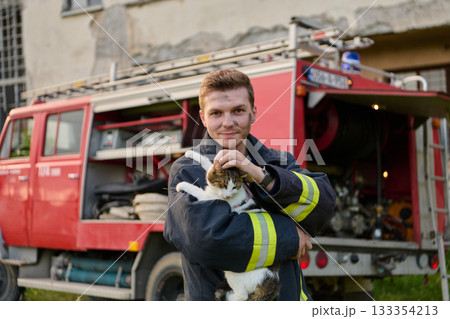Brave firefighter holding a rescued cat in front of a fire engine, showcasing heroism and compassion, a heartwarming scene of rescue and care, outdoor setting Brave firefighter holding a rescued cat in front of a fire engine, showcasing heroism and compassion, a heartwarming scene of rescue and care, outdoor setting 133354213