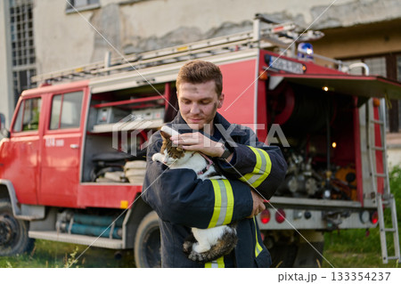 Brave firefighter holding a rescued cat in front of a fire engine, showcasing heroism and compassion, a heartwarming scene of rescue and care, outdoor setting 133354237