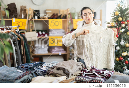 Armenian girl near showcase pick out and buying sweater, New Year eve 133356036