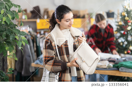 Armenian woman stands in a shop decorated for Christmas and chooses a handbag Armenian woman stands in a shop decorated for Christmas and chooses a handbag 133356041