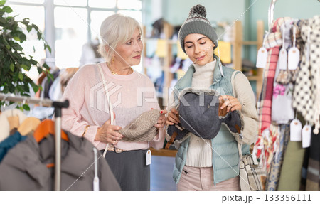 Elderly mother and her adult daughter choose together warm hat in clothing store 133356111