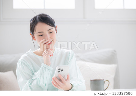 スマホ持つ女性が笑顔で幸せ感じる室内のかわいい日本人 問い合わせなどで考える よくある質問のイメージ スマホ持つ女性が笑顔で幸せ感じる室内のかわいい日本人 問い合わせなどで考える よくある質問のイメージ 133357590