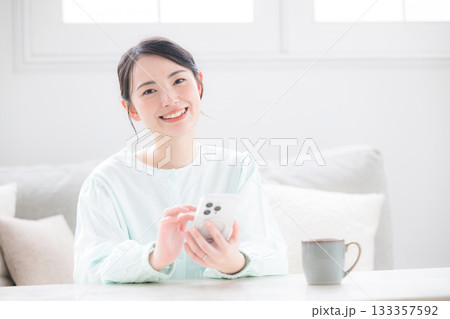スマホ持つ女性が笑顔で幸せ感じる室内のかわいい日本人　問い合わせなどで考える　よくある質問のイメージ 133357592