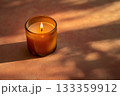 A lit candle placed inside a glass container, resting on a table. AI-generated content. 133359912