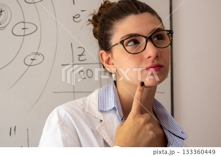 Teacher thinking and analyzing complex scientific problems on whiteboard, wearing a lab coat and glasses in a university or school classroom Teacher thinking and analyzing complex scientific problems on whiteboard, wearing a lab coat and glasses in a university or school classroom 133360449