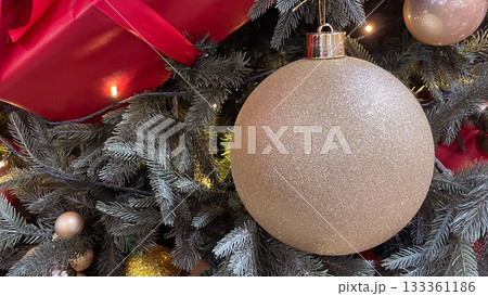 Large glittering gold Christmas bauble with a gift and pine needles background. Copy space. 133361186