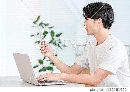 家のリビングでスマホとパソコンを使いテレワークする若いアジア人男性(悩む,考える,トラブル) 家のリビングでスマホとパソコンを使いテレワークする若いアジア人男性(悩む,考える,トラブル) 133361432