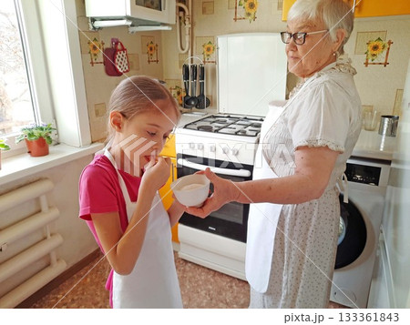 A grandmother and her granddaughter set out the necessary ingredients for cooking on the table. A grandmother and her granddaughter set out the necessary ingredients for cooking on the table. 133361843