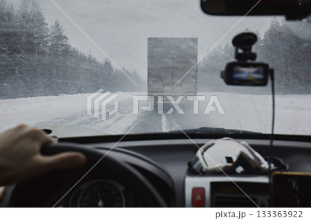 View from the eyes of the driver, from the windshield of the car on a winter road during a snowfall. Dangerous driving, snow is flying from the truck 133363922