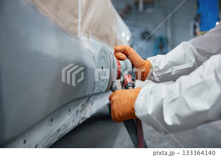 Technician sanding car body panel with orbital sander 133364140