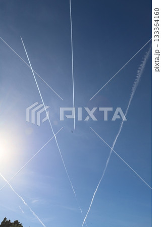 Contrails from aircraft create dynamic patterns in the clear blue sky, with sunlight illuminating the scene, showcasing the beauty of aviation and nature combined 133364160