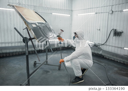 A technician spray-painting car hood inside a controlled automotive spray booth 133364190