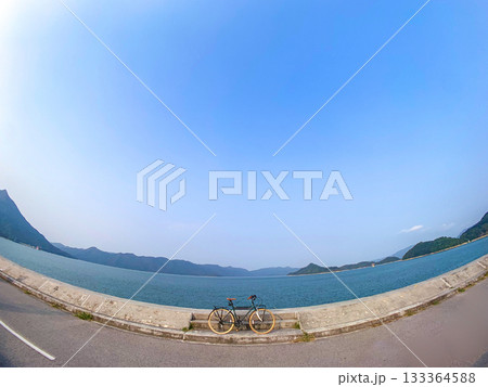 A bicycle sits on the side of the road with a stunning view of the water and mountains in the distance A bicycle sits on the side of the road with a stunning view of the water and mountains in the distance 133364588