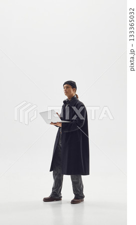 Stylish man in long coat using laptop symbolizing modern creative work and urban fashion confidence 133365032