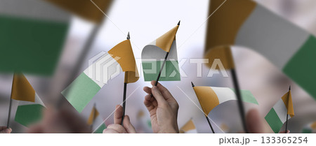 Cote dIvoire flags in their hands on a blurred urban background Cote dIvoire flags in their hands on a blurred urban background 133365254