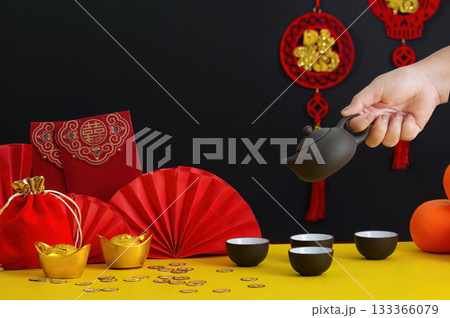 Lunar New Year tea ceremony. Hand pouring tea into cups with festive decor. Lunar New Year tea ceremony. Hand pouring tea into cups with festive decor. 133366079